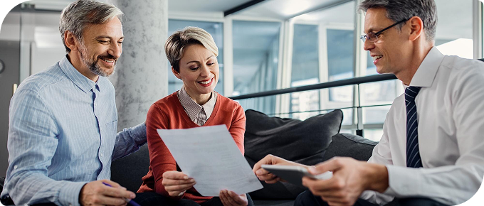 Smiling couple sitting with a financial advisor, reviewing a document together in a modern office setting